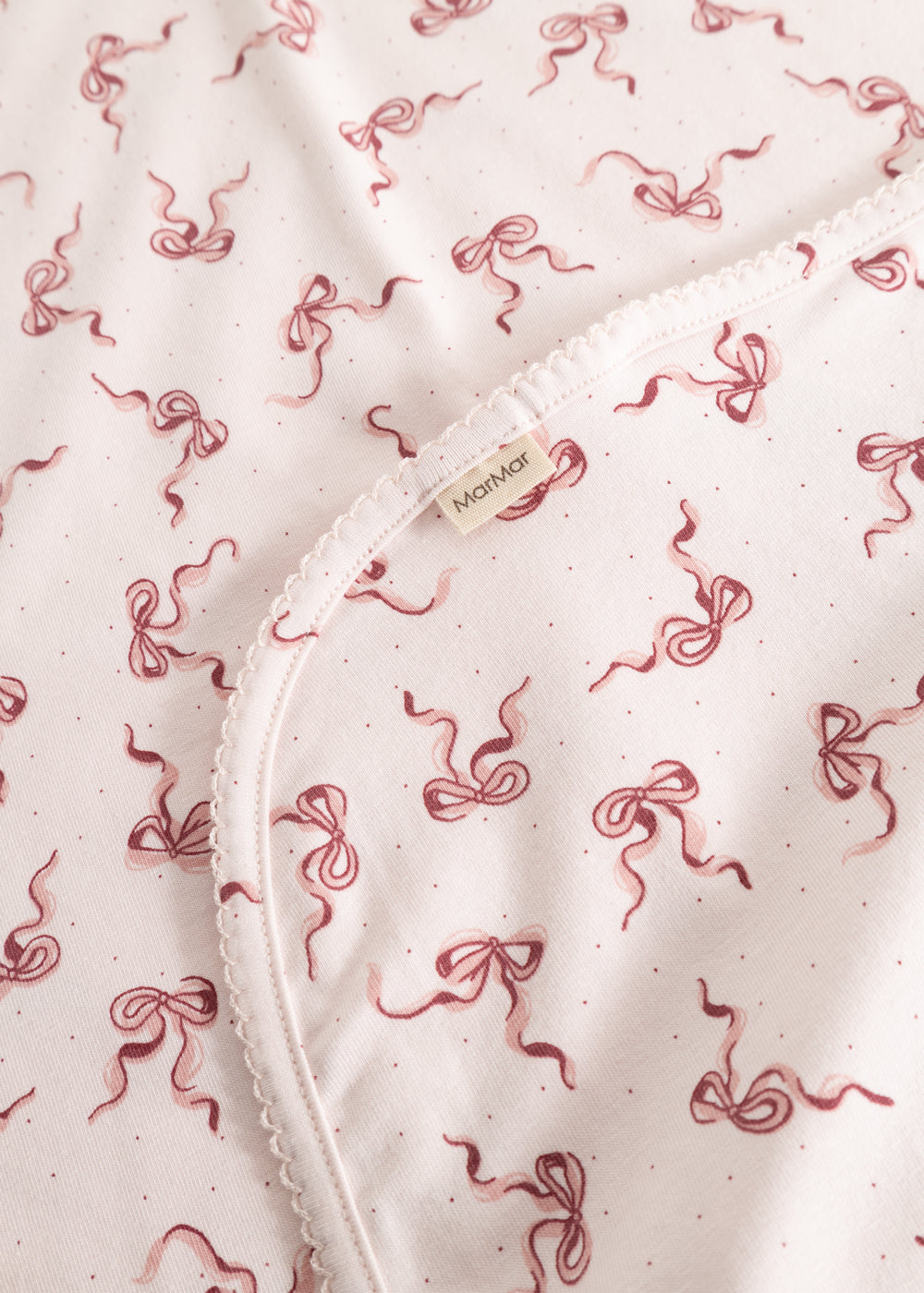 Carpet with bow pattern, reddish-pink on light background, edge and label