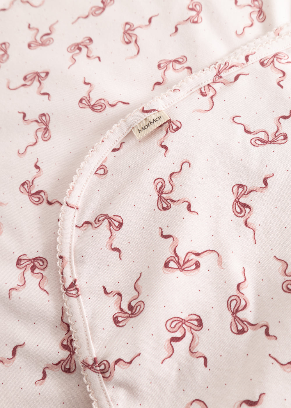 Close-up of carpet: light flat surface with red bow pattern and edge stitching.
