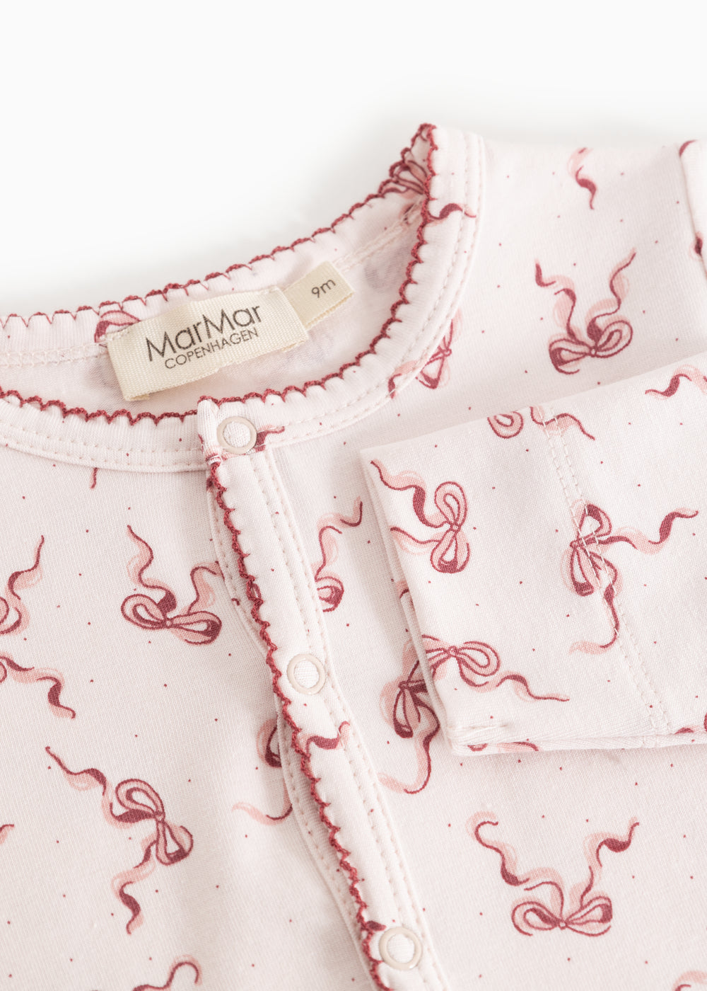 White jumpsuit with pink bow pattern, button and zipper closure at the neck