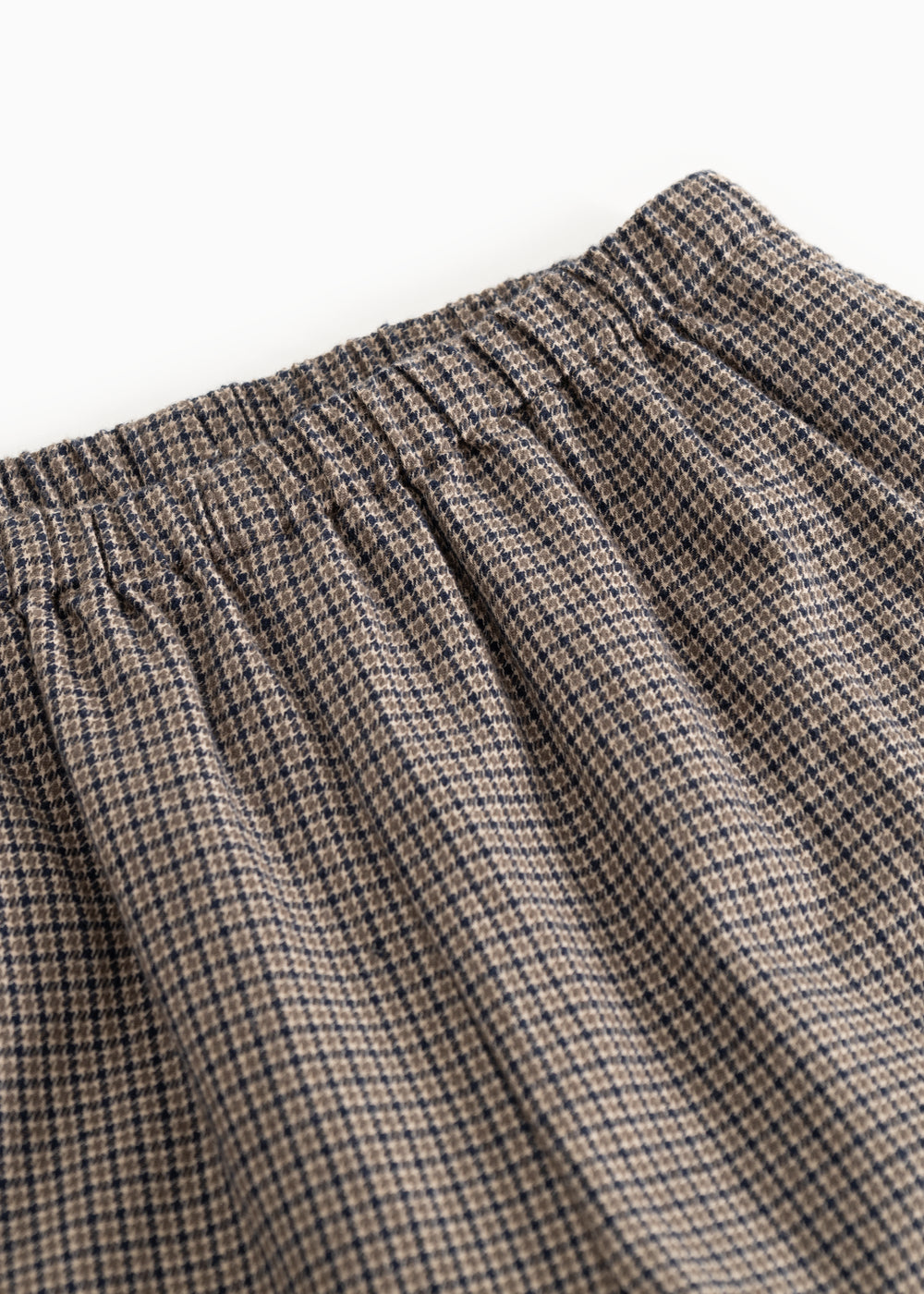 Detail of houndstooth trousers: elastic waistband and pleats at the waist.