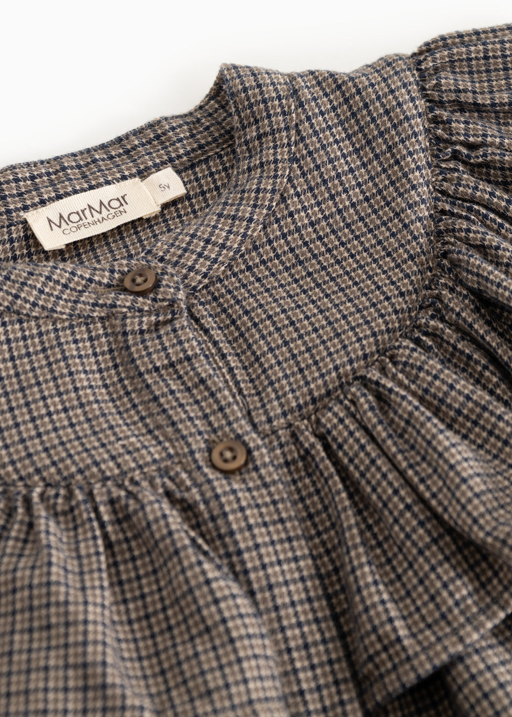 Children's dress with pied de poule pattern, button placket, and ruffle collar with textile label at the neck.