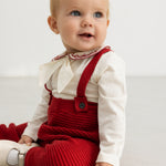 Red knitted overalls for baby, seen while the child is sitting