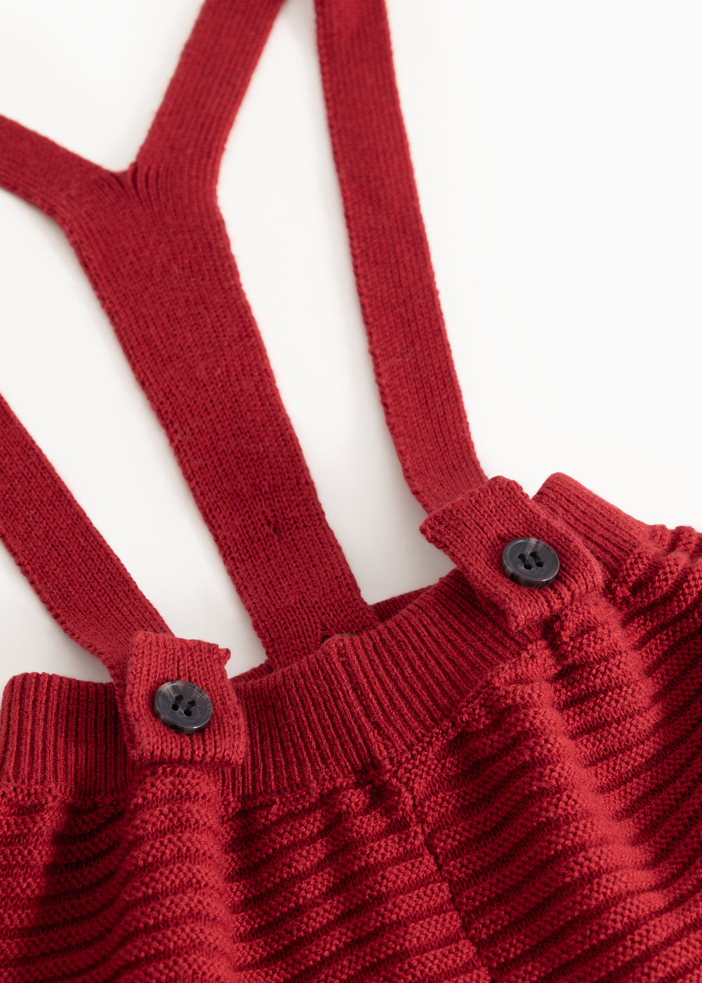 Detail: red knitted suspenders with two buttons on the suspender straps