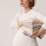 Pregnant woman wearing a white long-sleeved t-shirt and holding folded clothing.