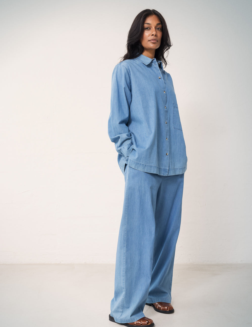Woman wearing a blue denim shirt and loose denim pants.