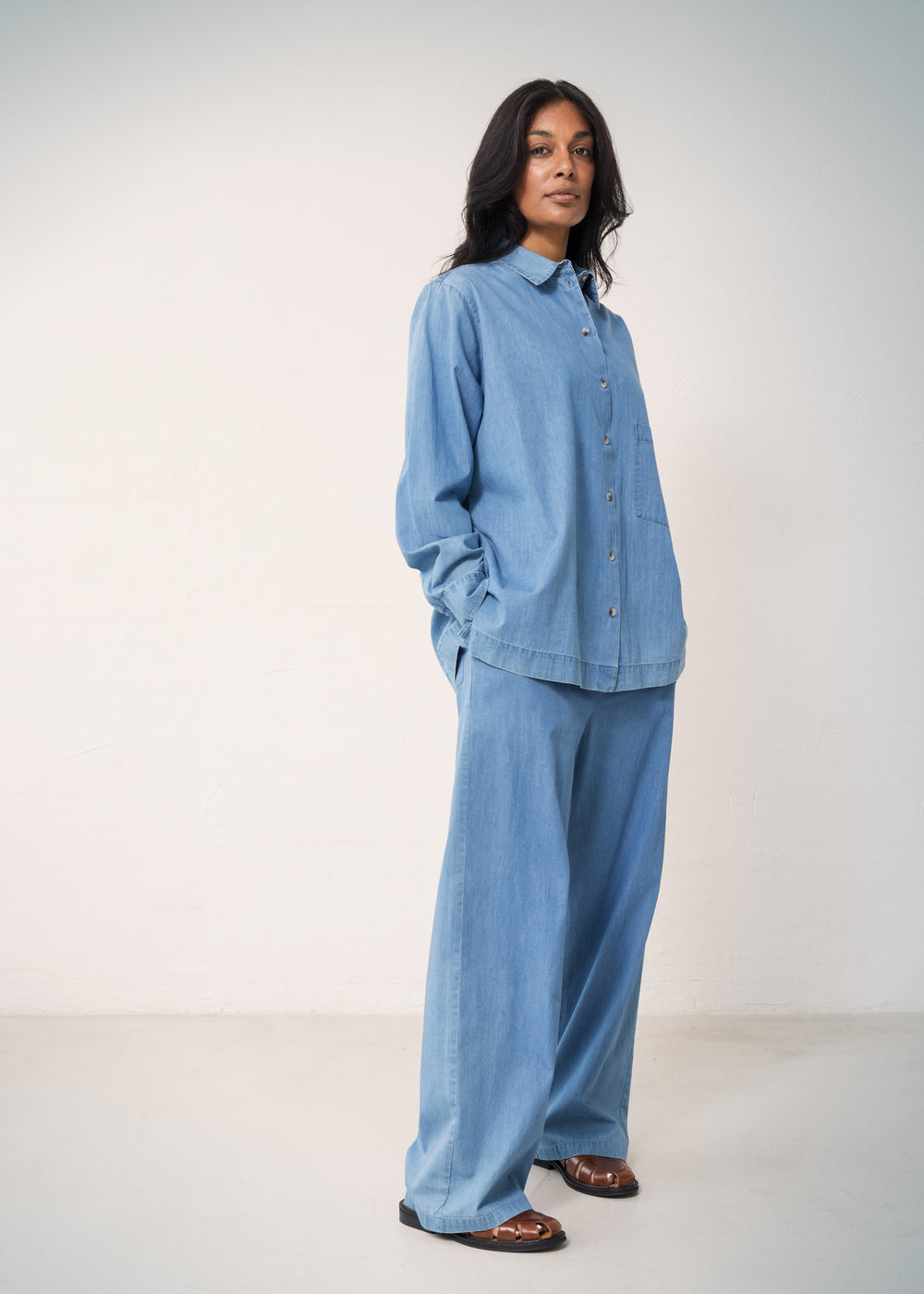 Woman wearing a blue denim shirt and loose denim pants.