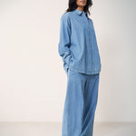 Woman wearing a blue denim shirt and loose denim pants.