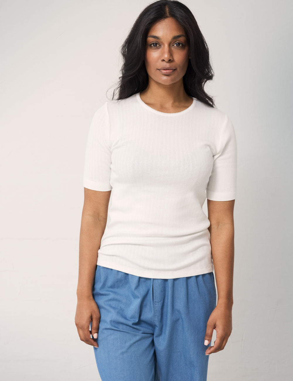 Woman wearing a white ribbed T-shirt with short sleeves and denim pants.