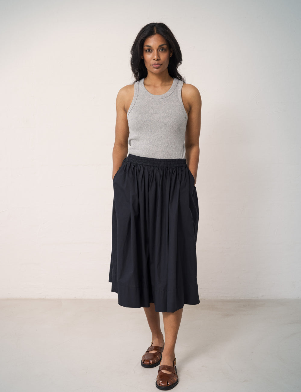 Woman wearing a black skirt with elastic in the waist and a slightly ruffled blouse and a gray tank top.