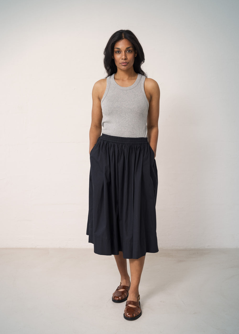 Woman wearing a black skirt with elastic in the waist and a slightly ruffled blouse and a gray tank top.