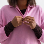 Pink polo with collar and button closure, short sleeves, visible black cuff underneath.