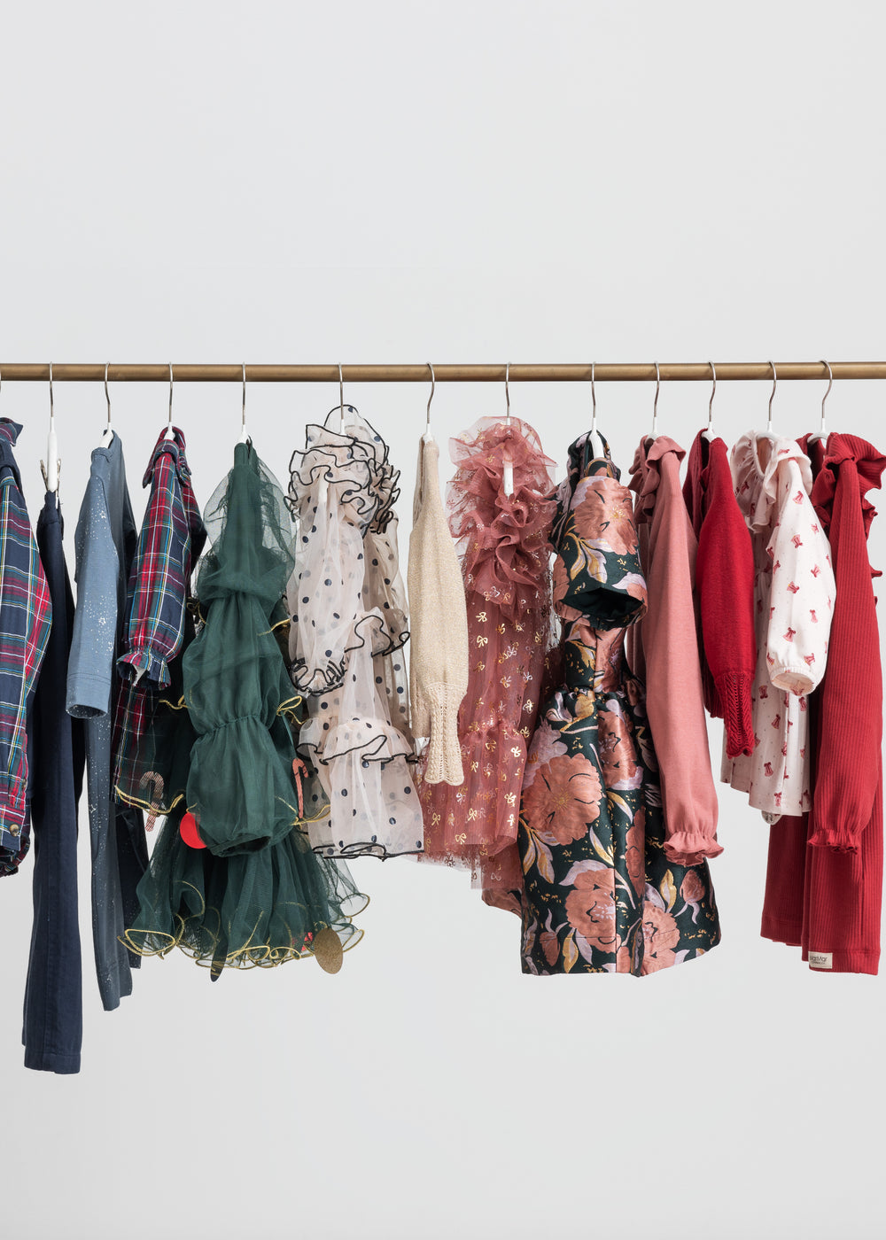Festtøj og julekjoler til børn i forskellige farver hængende på tøjstativ 