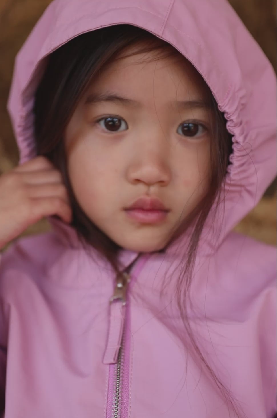 Barn i lyserød overgangsjakke med hætte tæt på ansigtet