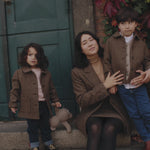 Mor og børn iført brune jakker foran grøn dør