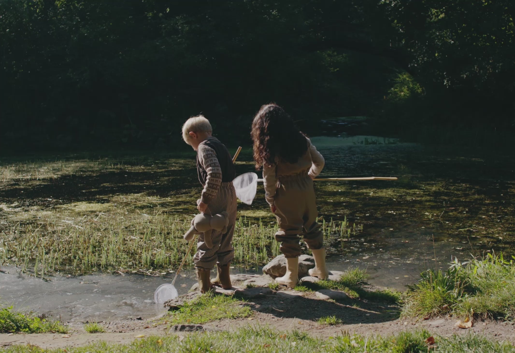 To børn leger udendørs i stribet regntøj ved vand