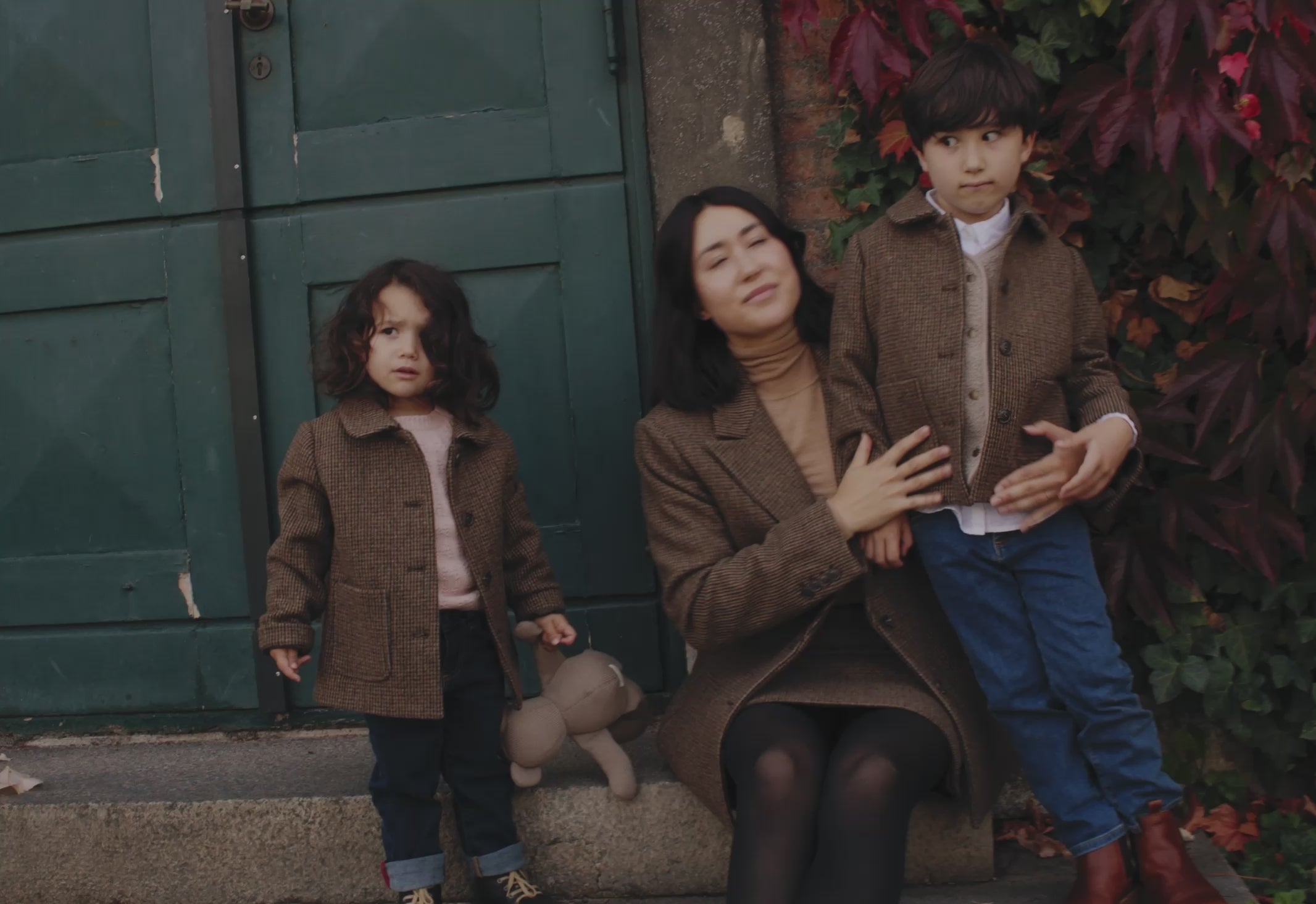 Mor og børn iført brune uldfrakker foran grøn dør
