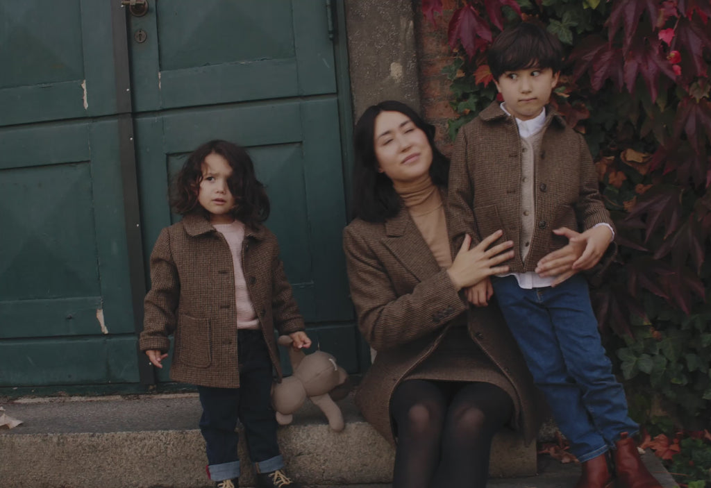 Mor og børn iført brune uldfrakker foran grøn dør