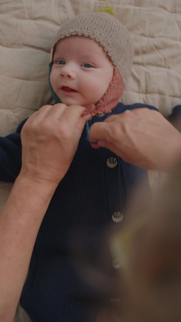 Baby får hjælp til at tage beige uldhue på